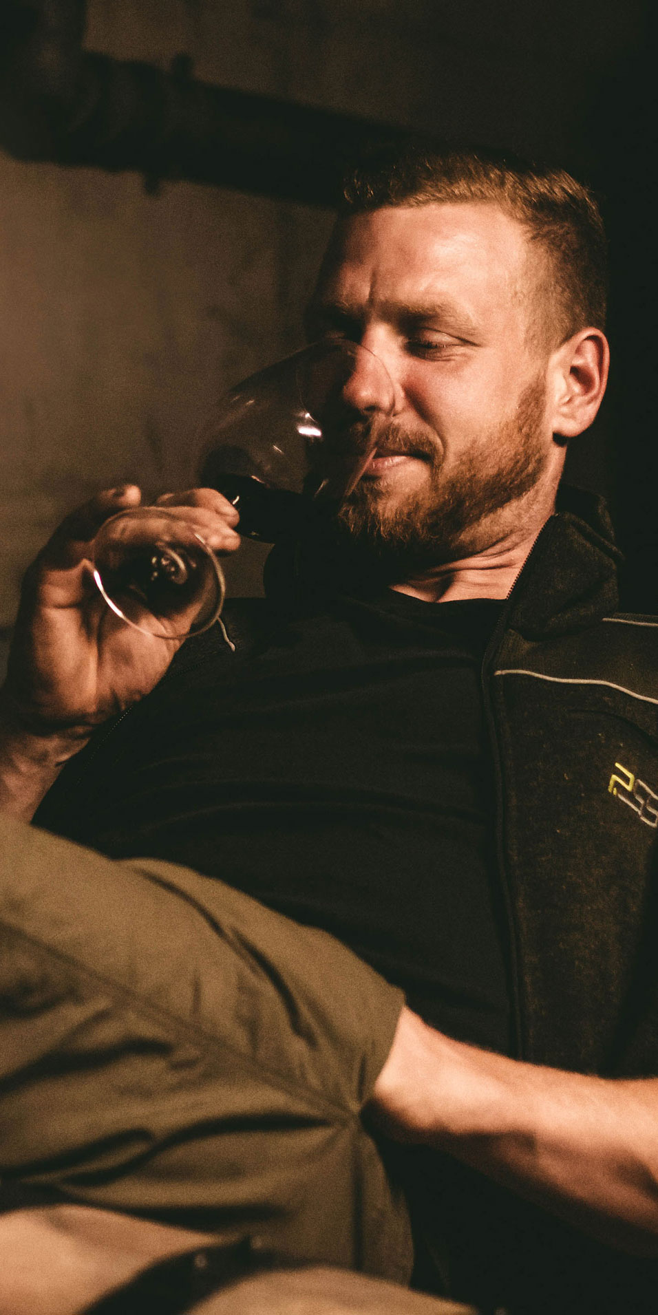 Daniel Schweizer liegt auf Holzfässern und riecht an einem Weinglas.